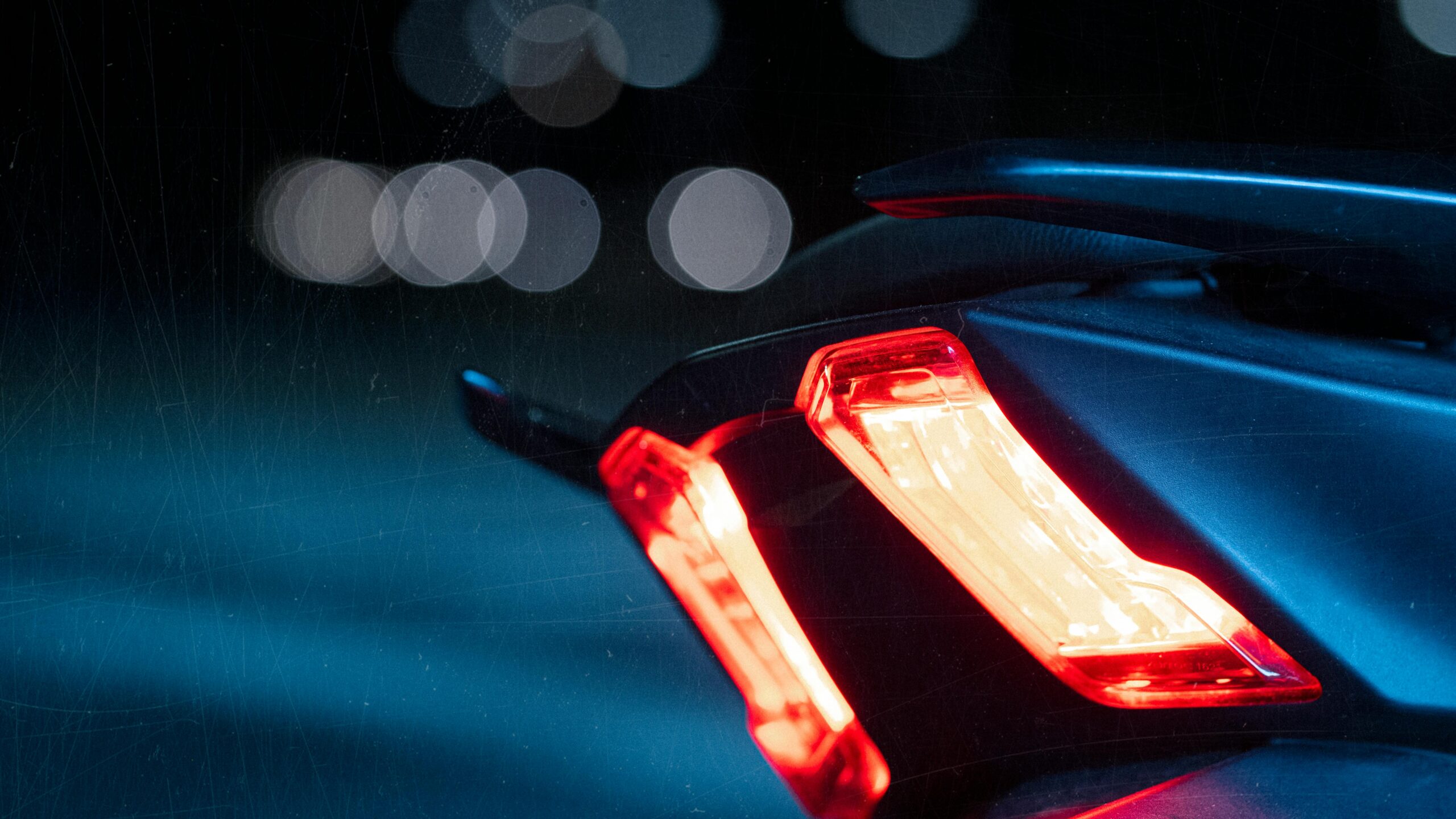 A detailed view of a motorcycle taillight glowing brightly against the dark night, showcasing vibrant bokeh.